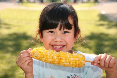 微笑的女孩拿着煮熟的玉米白天
